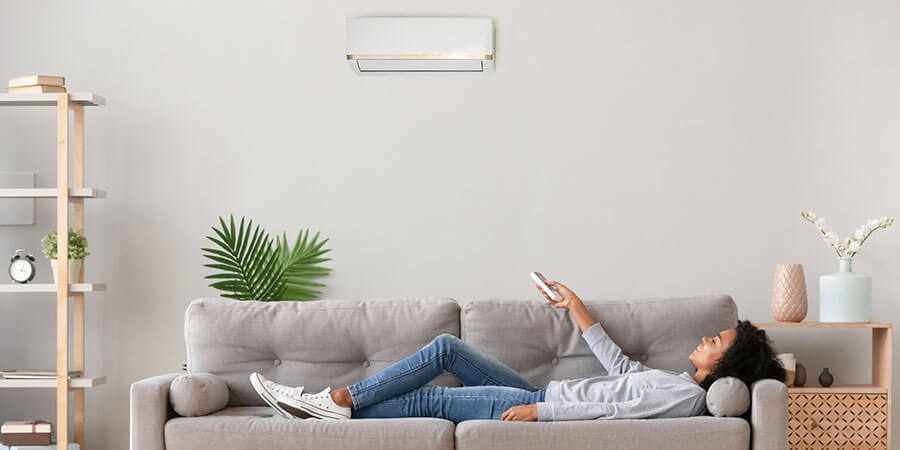 Woman relaxing on the couch while adjusting her ductless mini-split 
