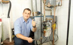 technician kneeling next to furnace and giving a thumbs up